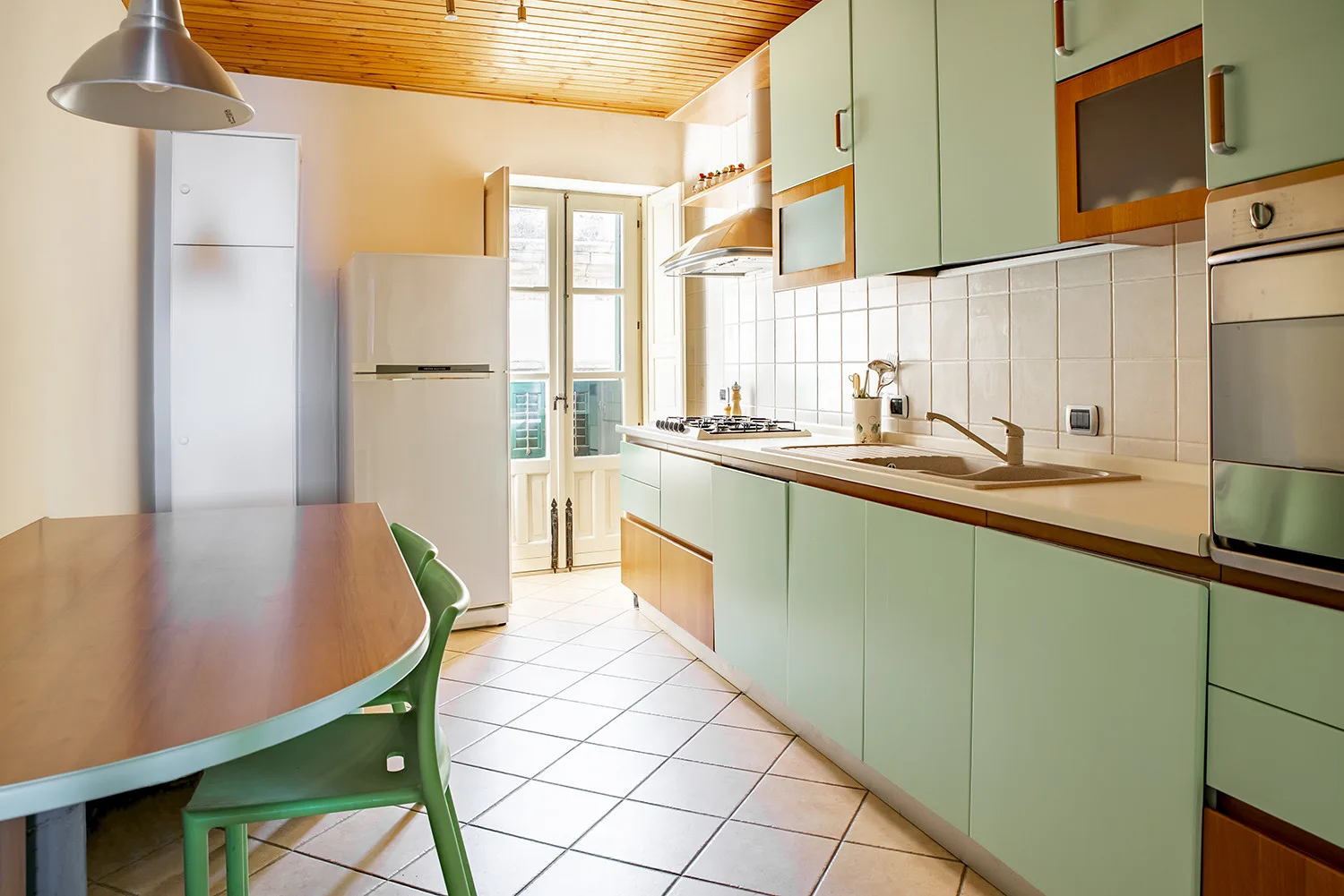 Una cocina luminosa con gabinetes verde claro y una mesa de comedor.