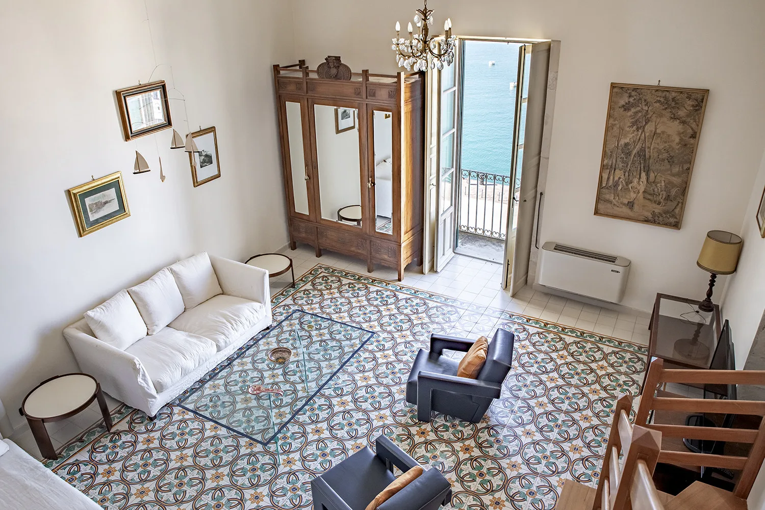 Una sala luminosa con asientos blancos, suelo de baldosas estampadas y una puerta abierta al balcón.