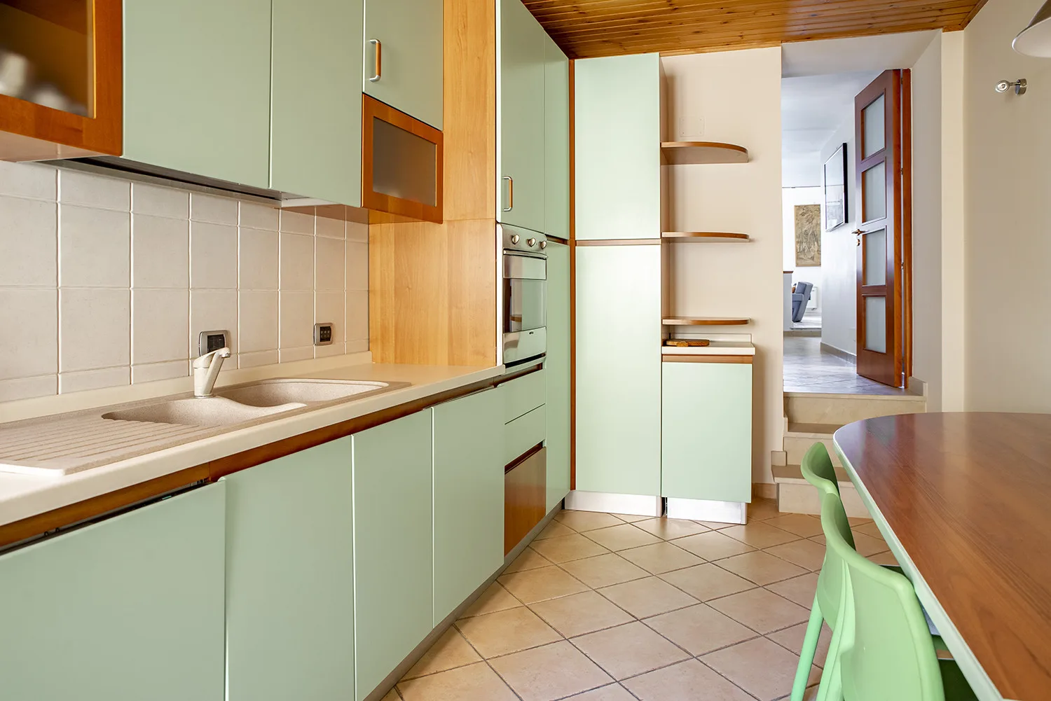 Una cocina con gabinetes verde claro, un fregadero y una mesa de comedor.