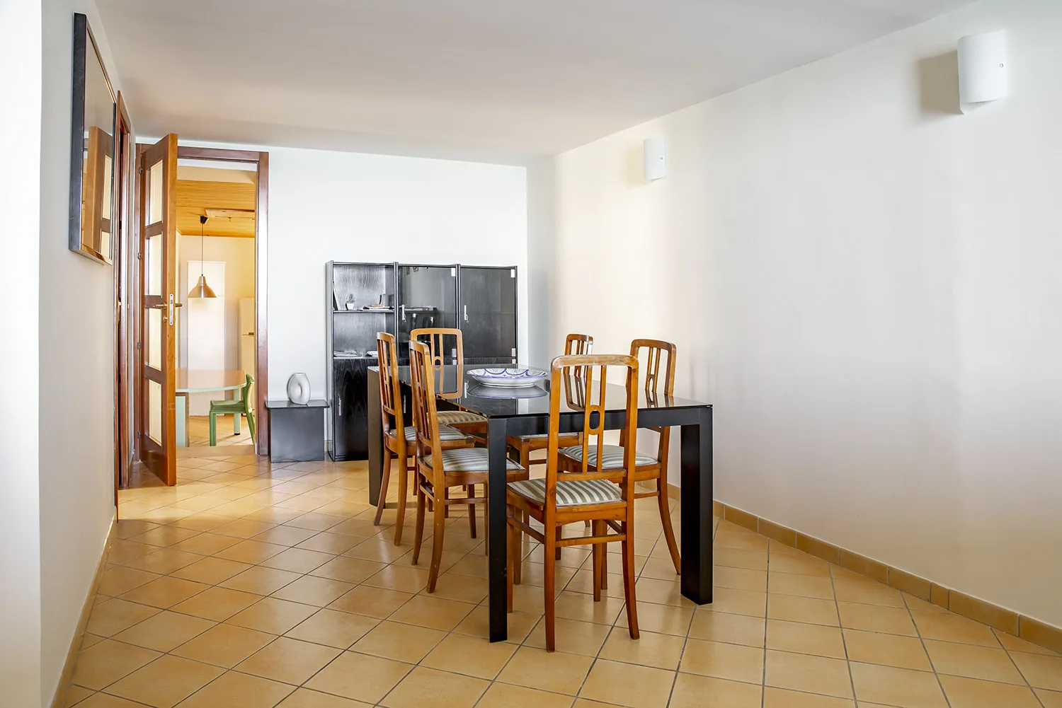Comedor con una mesa larga y asientos de madera junto a un armario con puertas de vidrio.