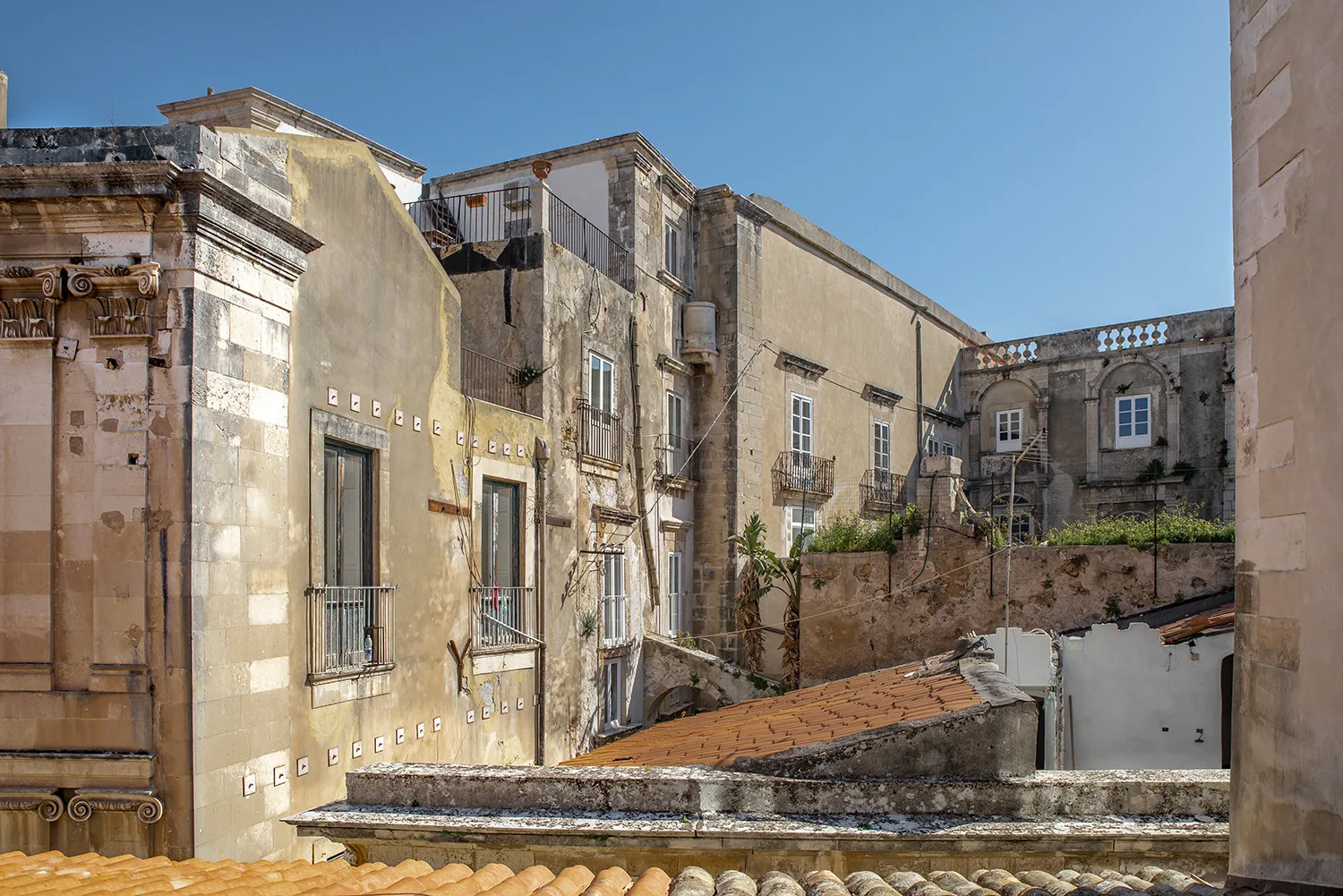 Edificios de piedra y tejados de tejas rodean un pequeño patio bajo un cielo despejado.