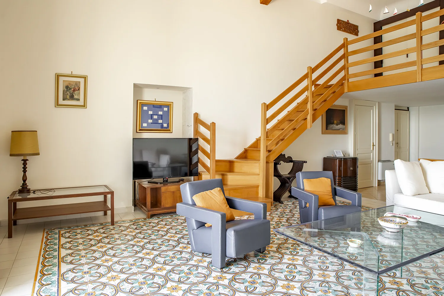 Una sala de estar con asientos, una mesa de centro de vidrio y una escalera de madera.