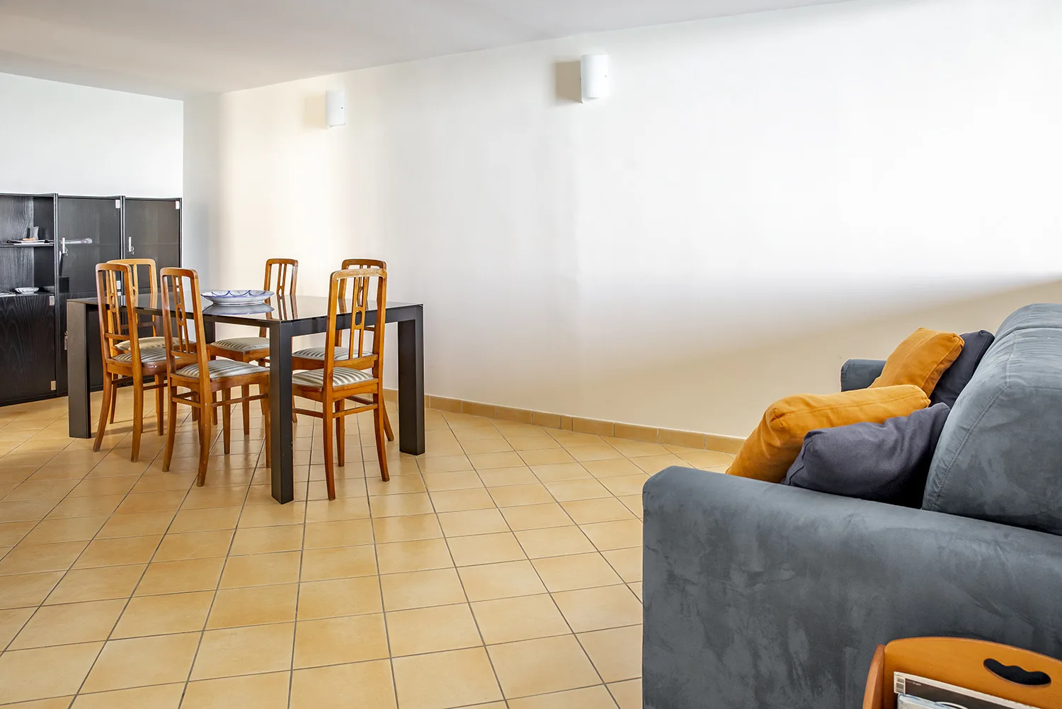 Una zona de comedor y estar con una mesa de madera y asientos grises.