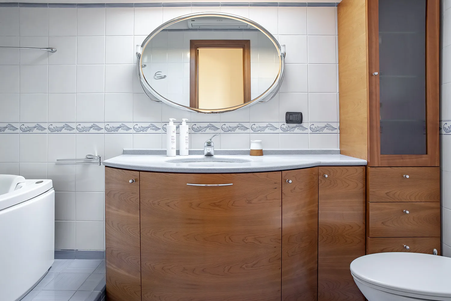 Un baño alicatado con tocador de madera, espejo ovalado e inodoro.