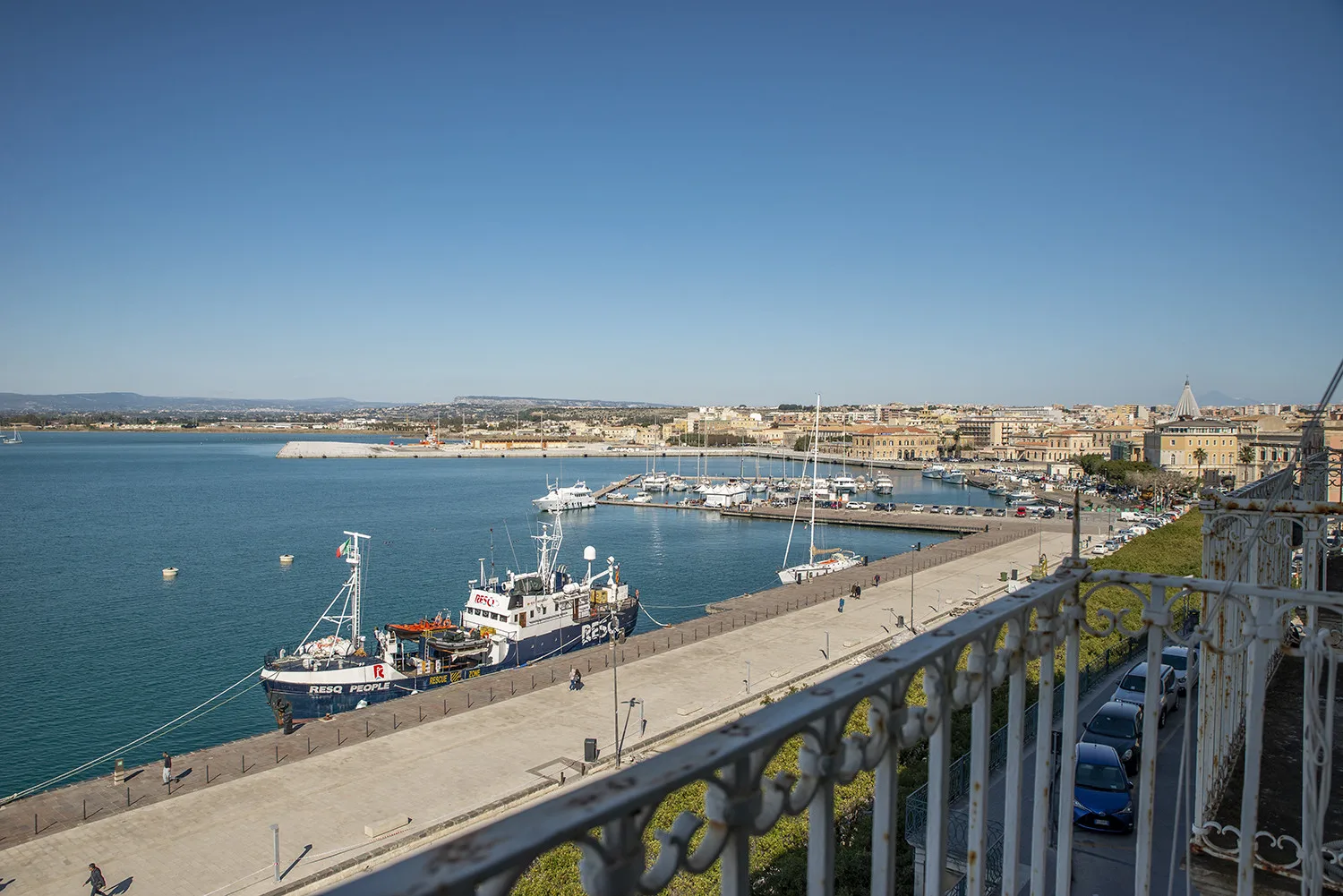 Un paseo junto al puerto da a barcos amarrados y aguas azules tranquilas.
