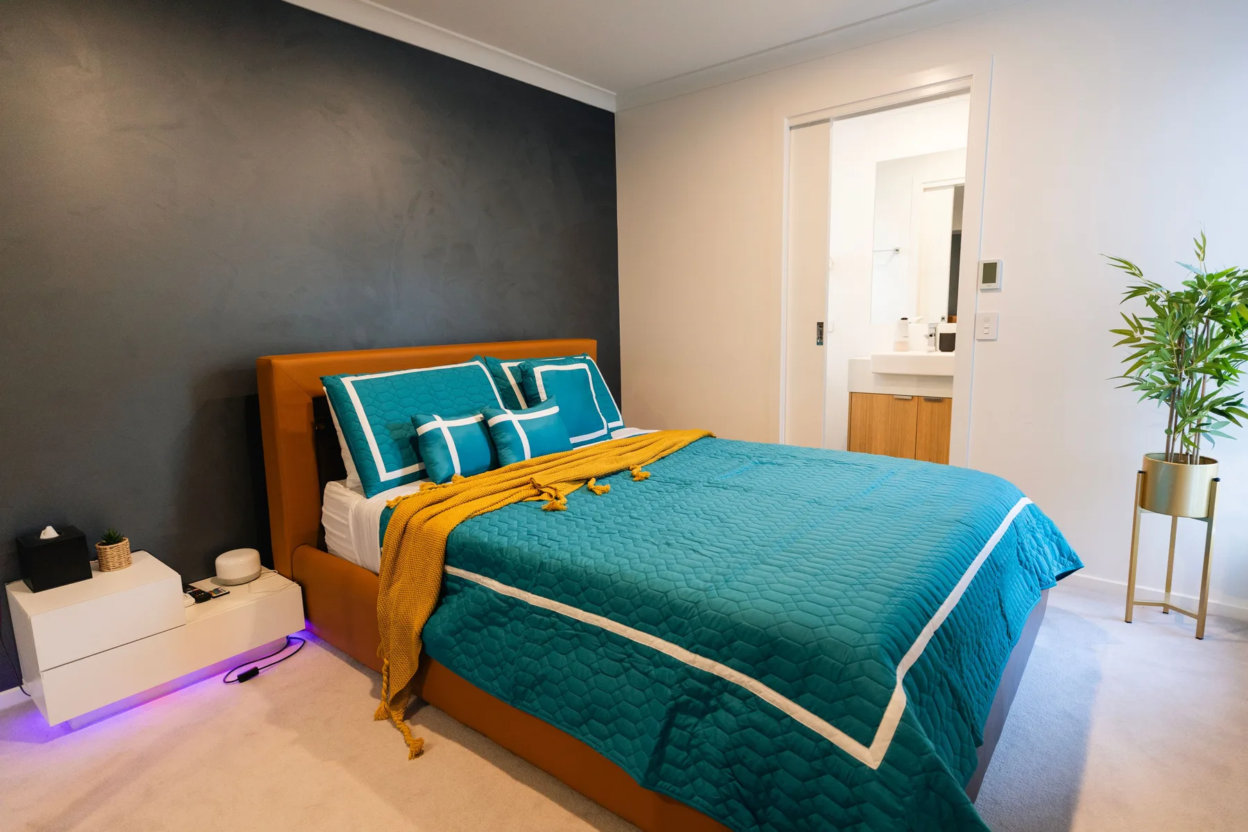 Un dormitorio con una cama vestida con ropa de cama turquesa y una pared oscura.