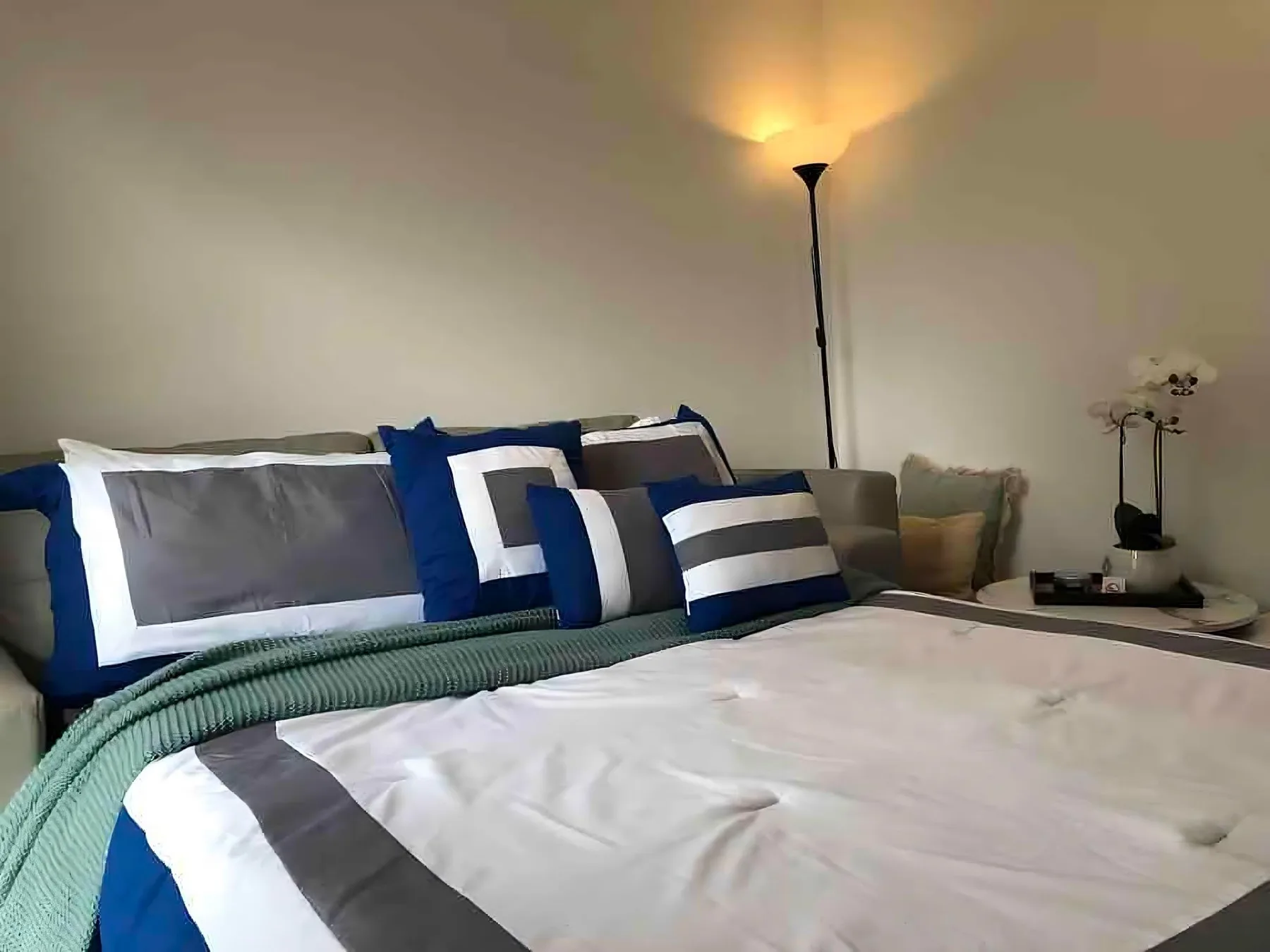 Un dormitorio con una cama bien hecha y una lámpara de pie al lado.