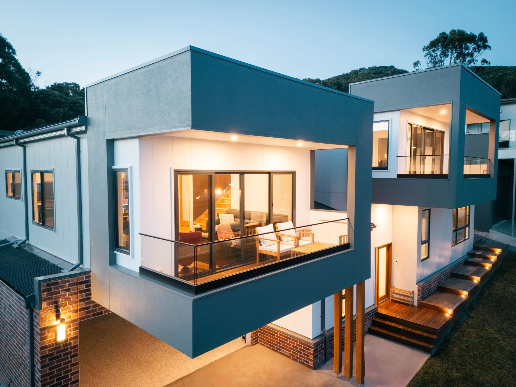 Exterior de una casa moderna con ventanas iluminadas y una pequeña terraza.