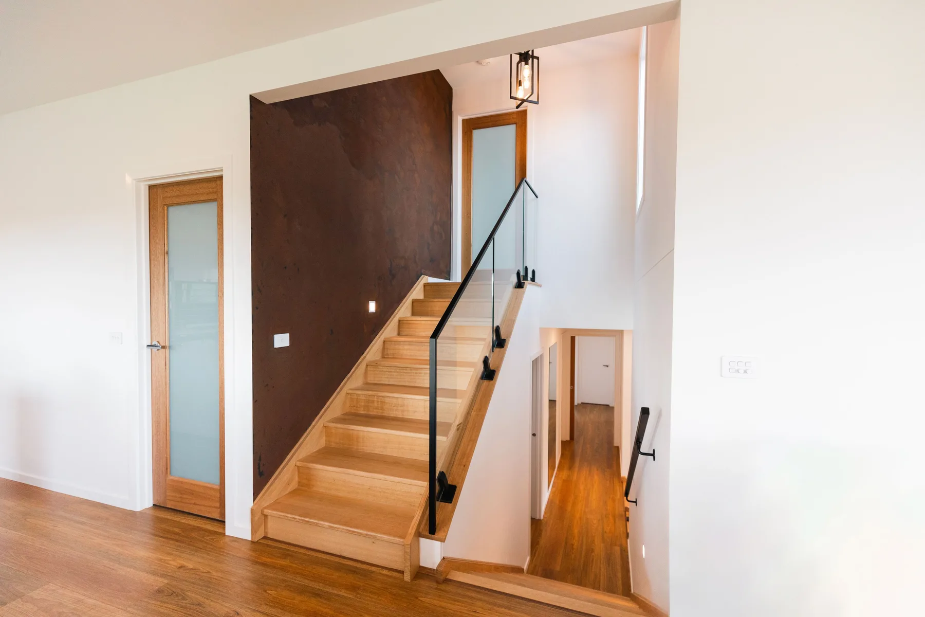 Una escalera de madera con barandilla negra sube junto a una pared oscura.