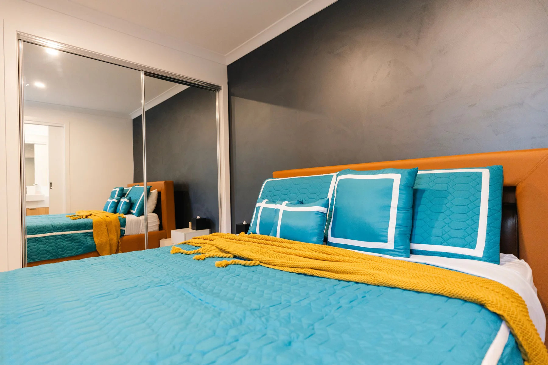 Dormitorio con ropa de cama turquesa y puertas de armario con espejo.