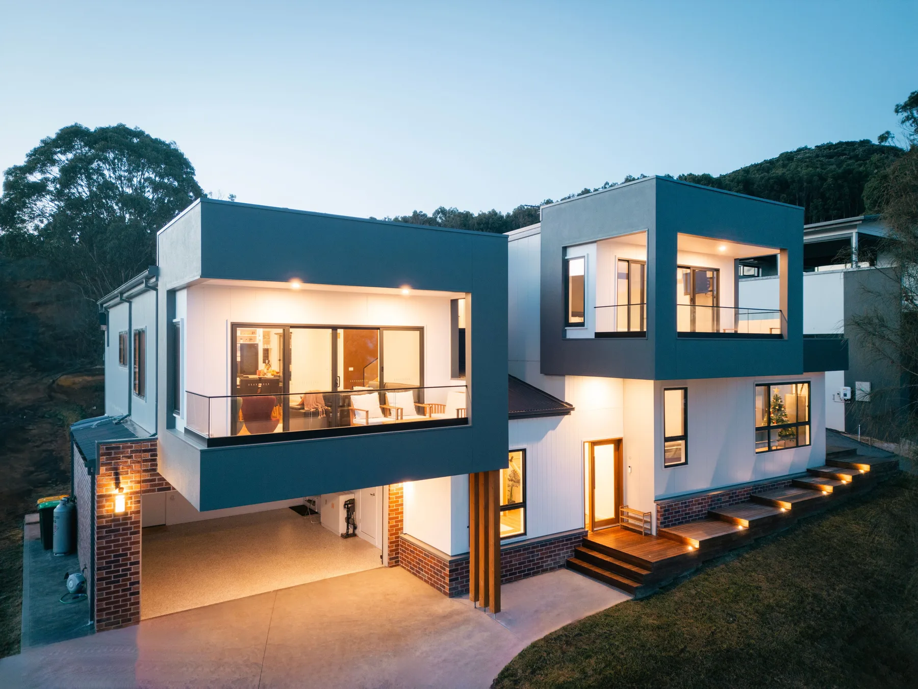 Una casa moderna de dos plantas con grandes ventanas y escalones exteriores iluminados.