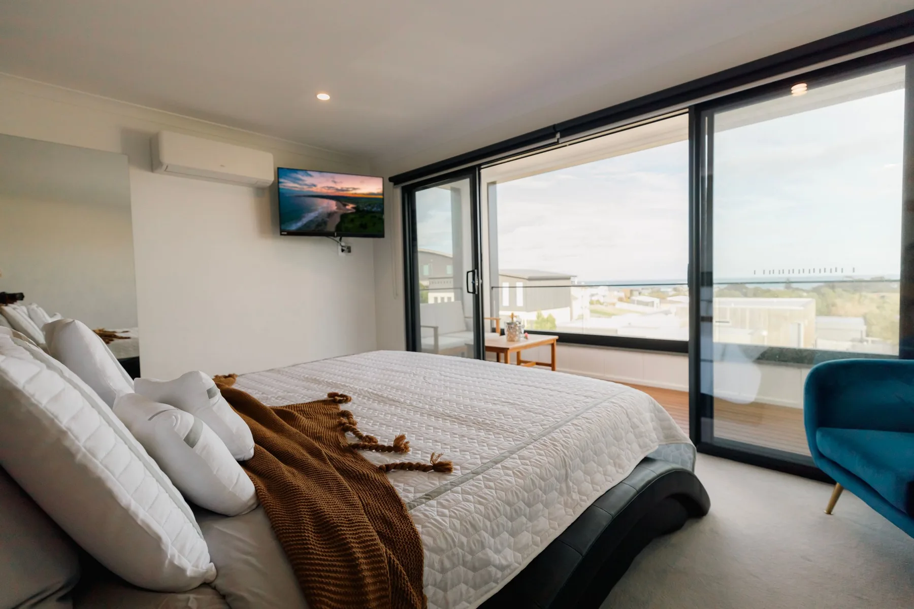Un dormitorio con una cama junto a grandes ventanas con vista a la costa.