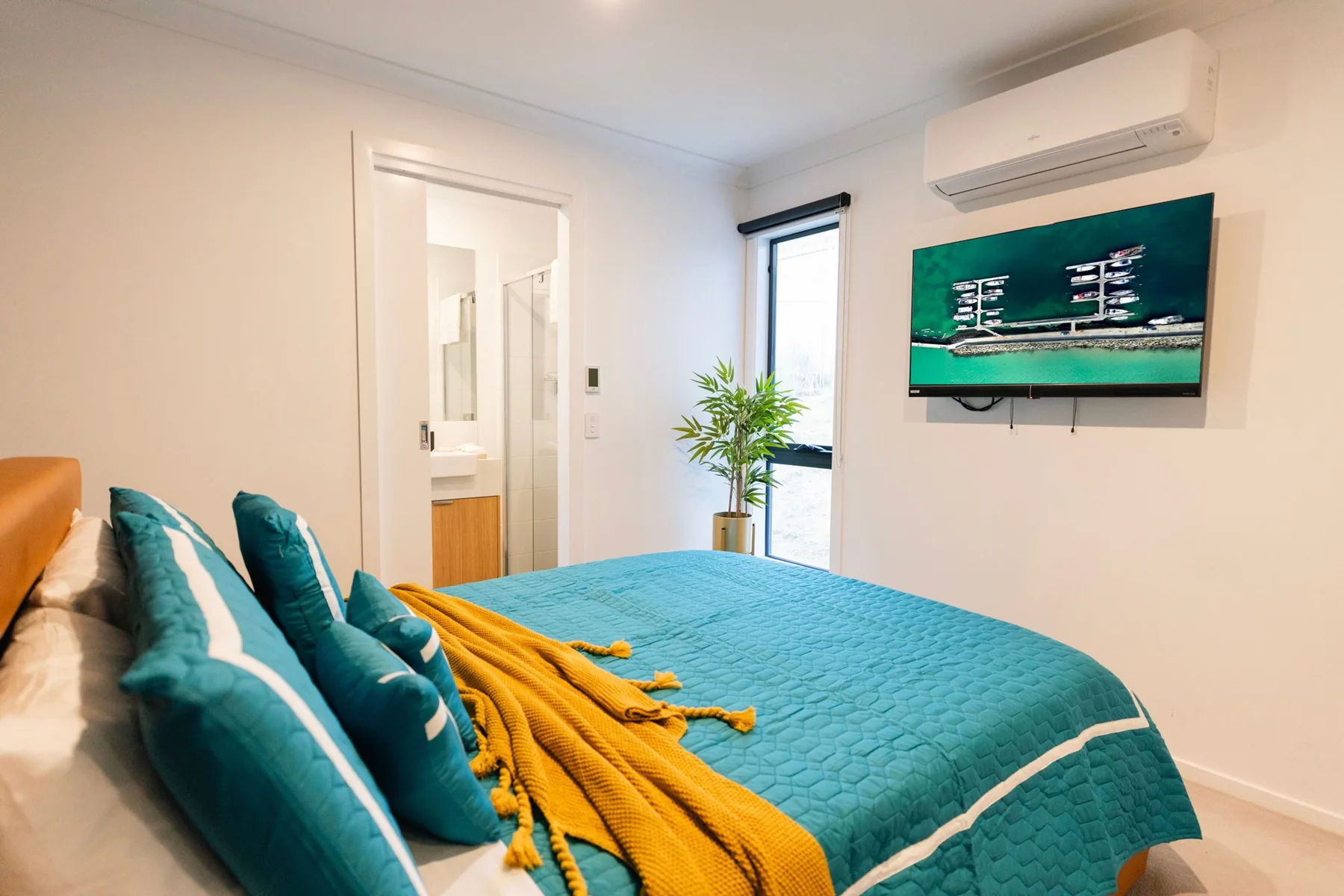 Dormitorio con una cama turquesa, cojines de colores y un televisor en la pared.