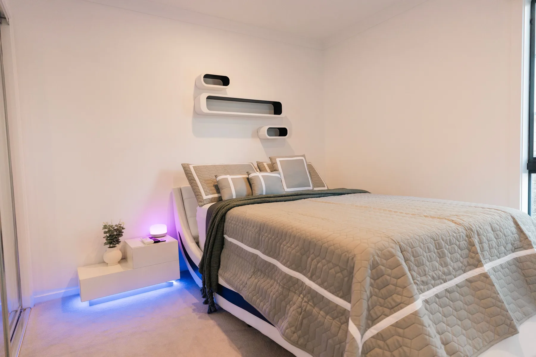 Un dormitorio con una cama, ropa de cama neutra y una mesita de noche.
