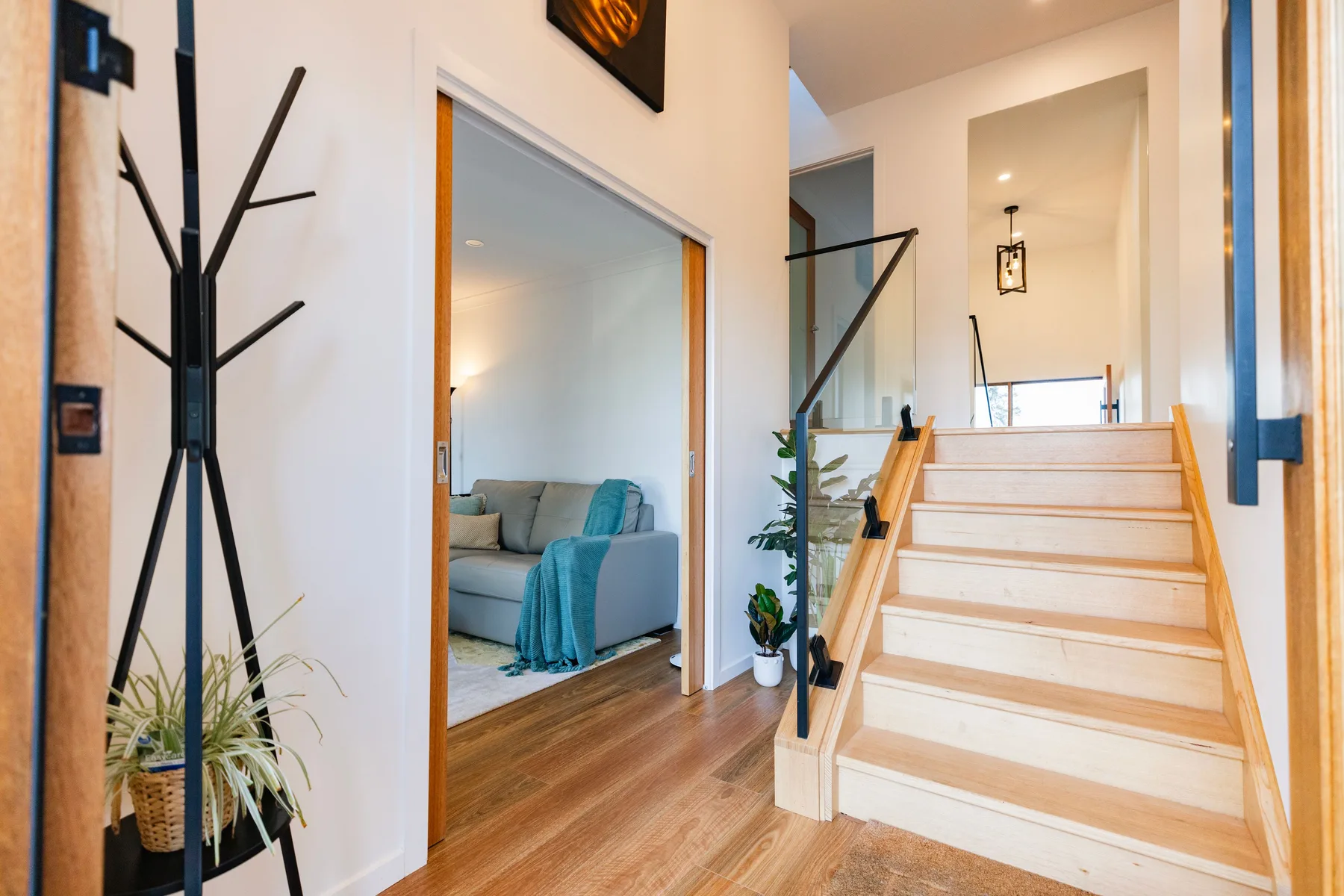 Un pasillo interior con escaleras de madera y una puerta abierta a una sala de estar.