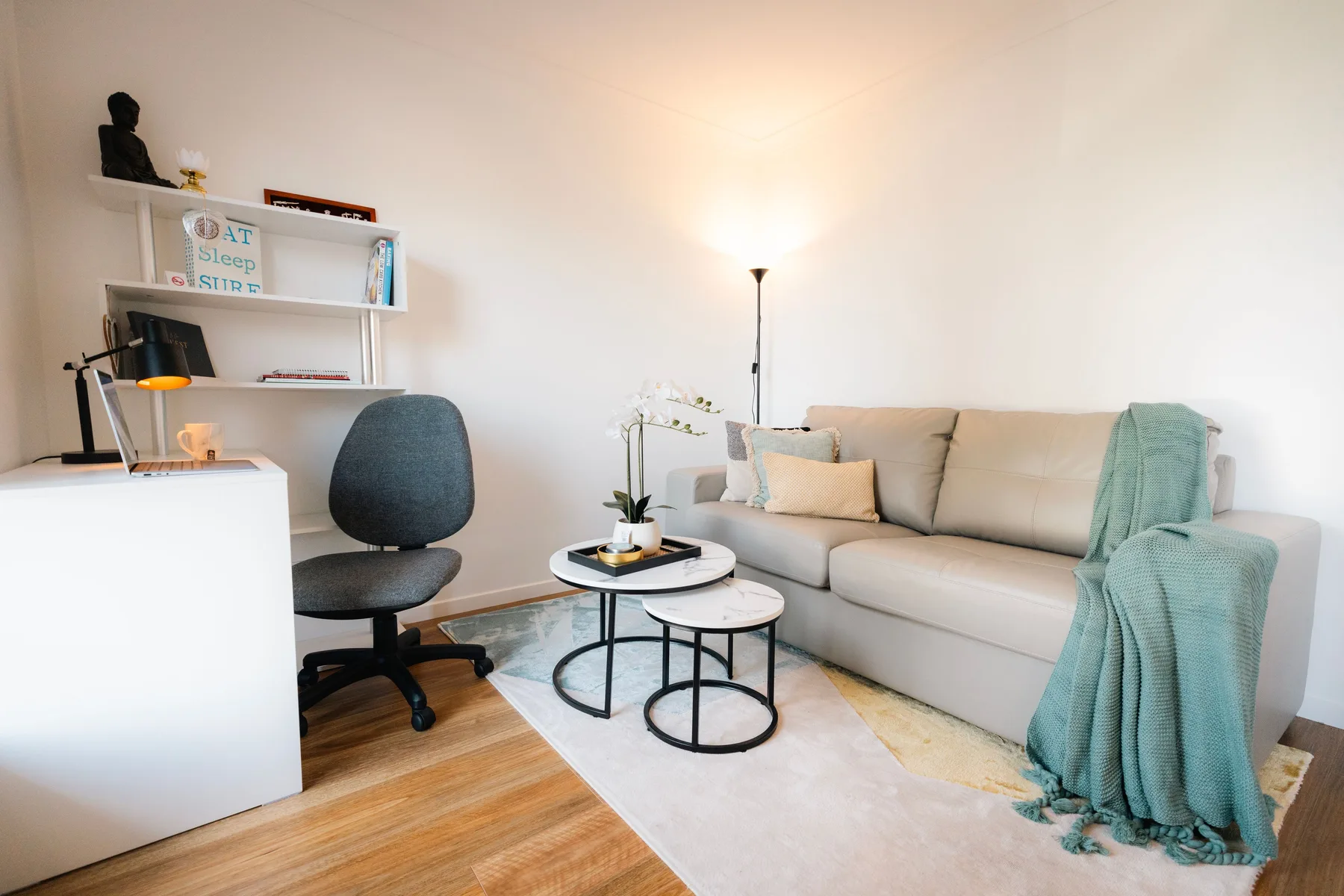 Una sala de estar luminosa con sofá, mesitas y escritorio.