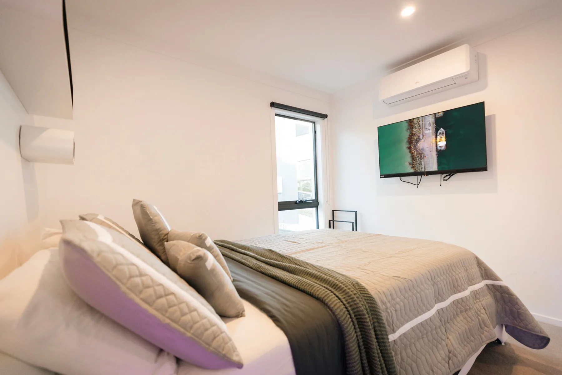 Un dormitorio con una cama bien tendida y un televisor montado en la pared.