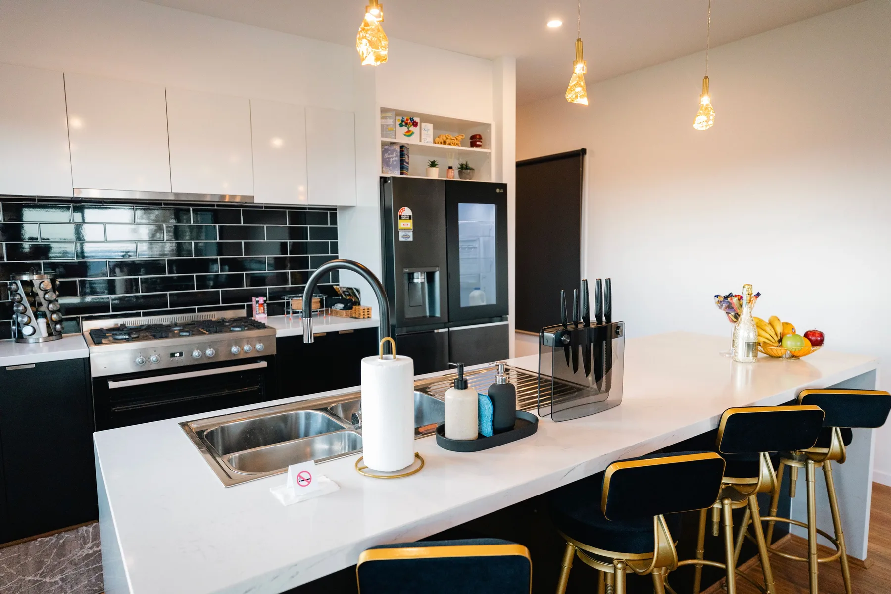 Una cocina moderna con una isla central, asientos de barra y un salpicadero negro brillante.