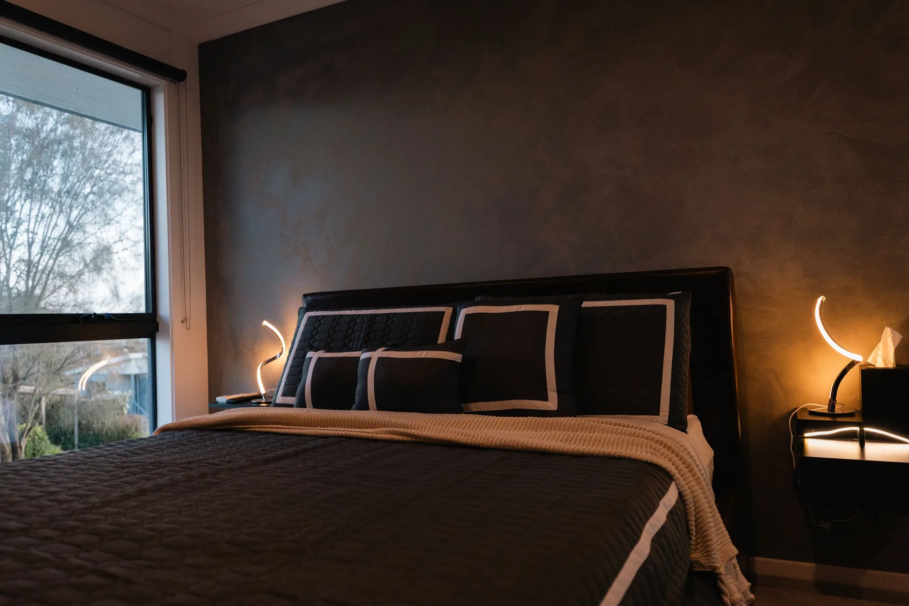 Un dormitorio con una cama bien hecha e iluminación cálida junto a la cama.