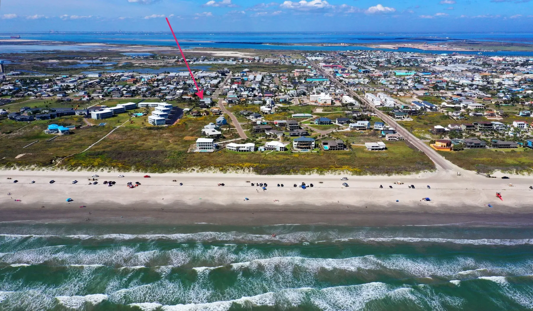 Vista aérea de un pueblo costero, con una playa de arena y el océano en primer plano.