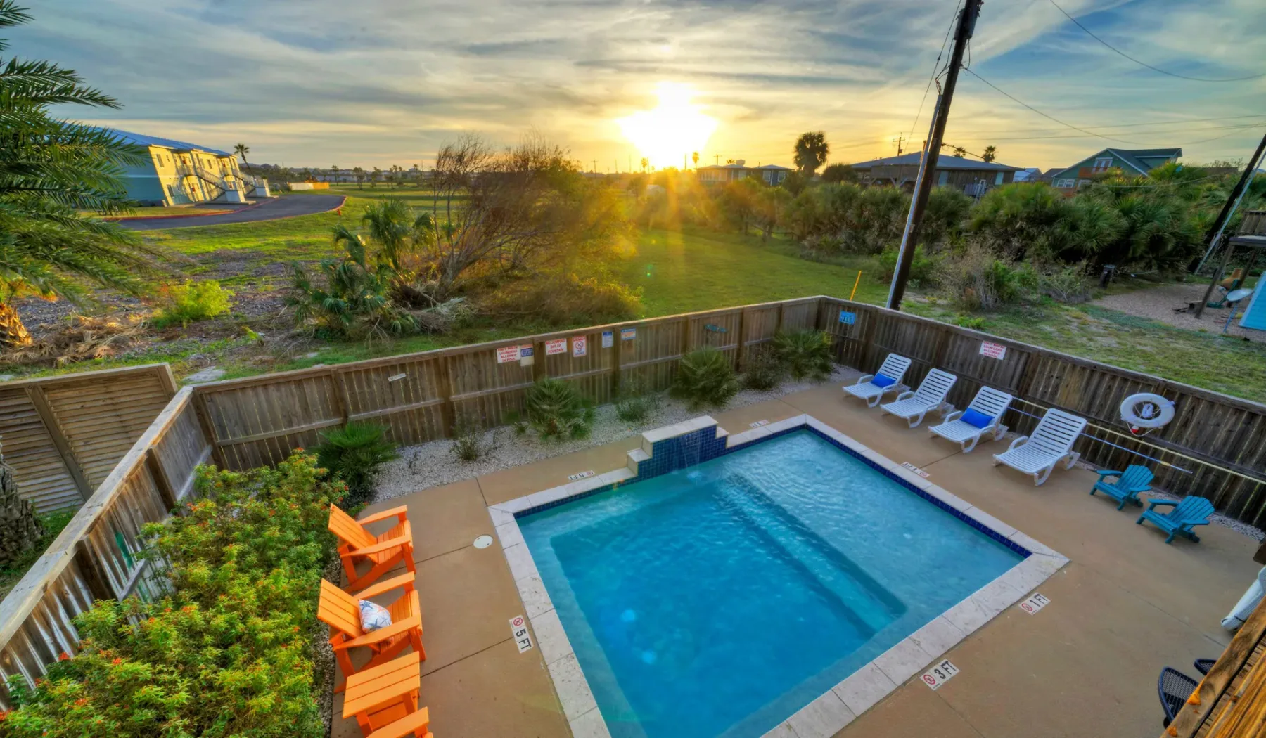 Una piscina al aire libre está junto a un patio cercado al atardecer.