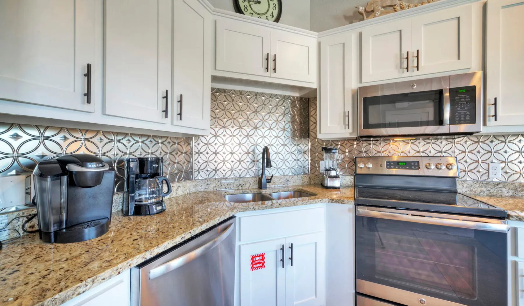 Una cocina luminosa con gabinetes blancos, salpicadero estampado y electrodomésticos de acero inoxidable.