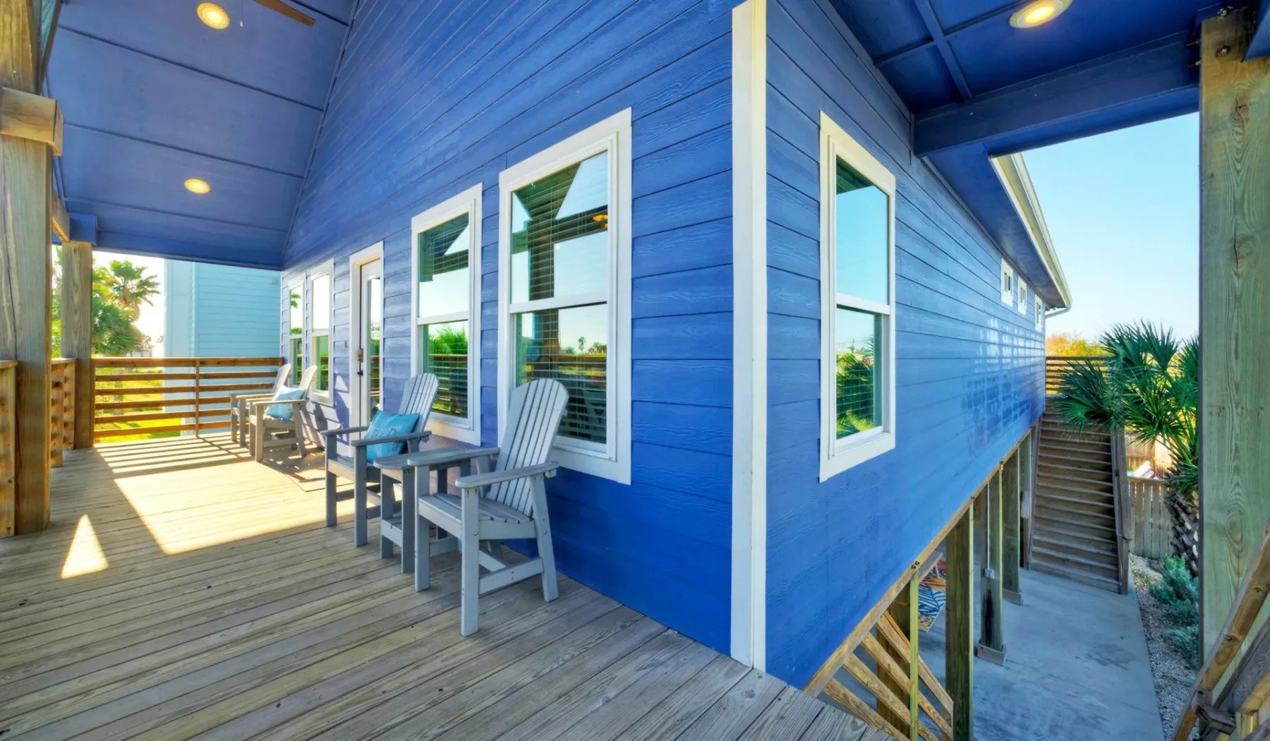 Una terraza de madera junto a un edificio azul con ventanas y asientos.