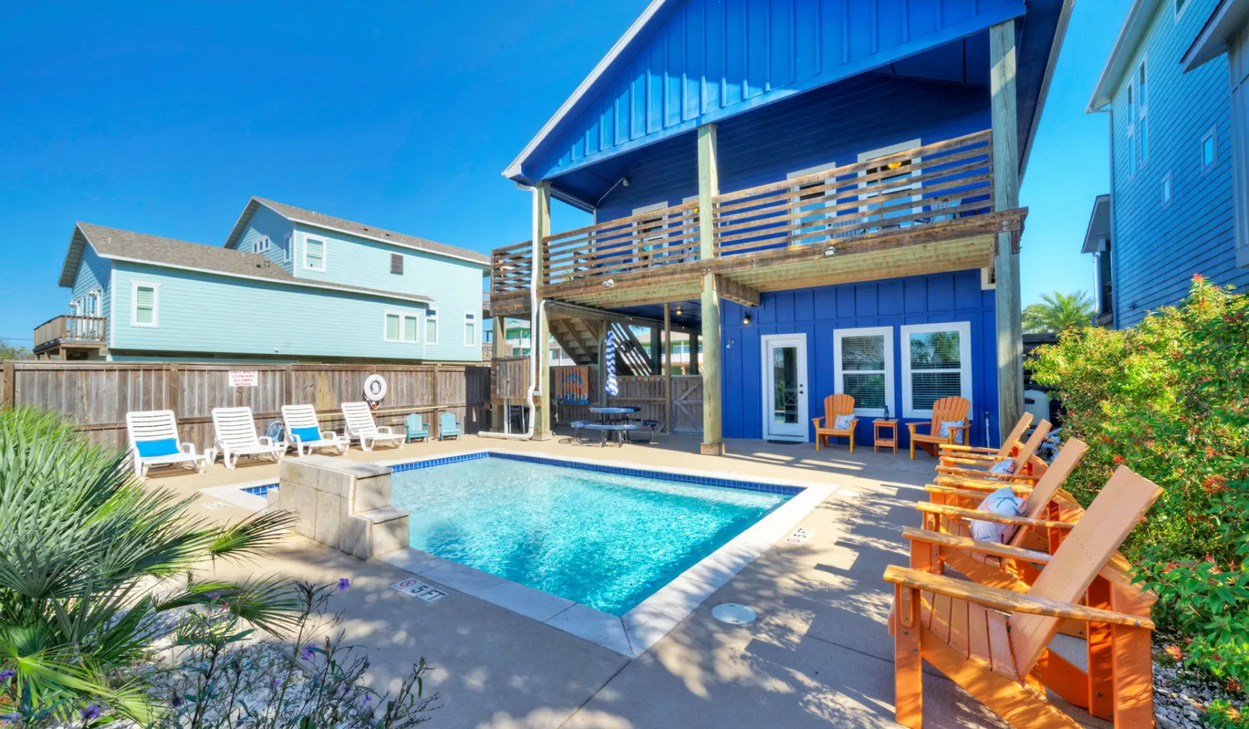 Una piscina en el patio está junto a una casa azul con asientos al aire libre.