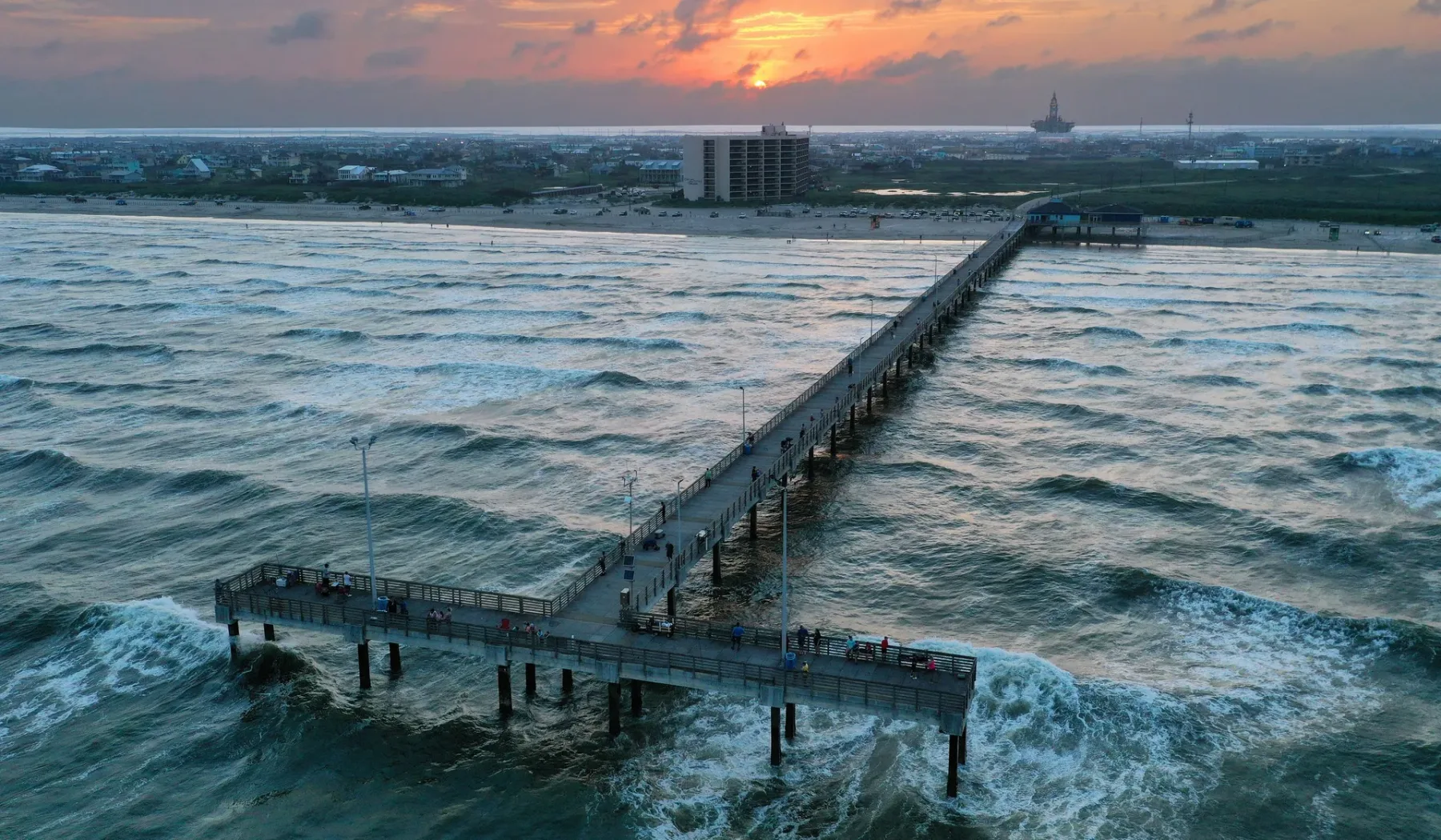 Un largo muelle se extiende sobre aguas agitadas bajo un cielo de atardecer colorido.