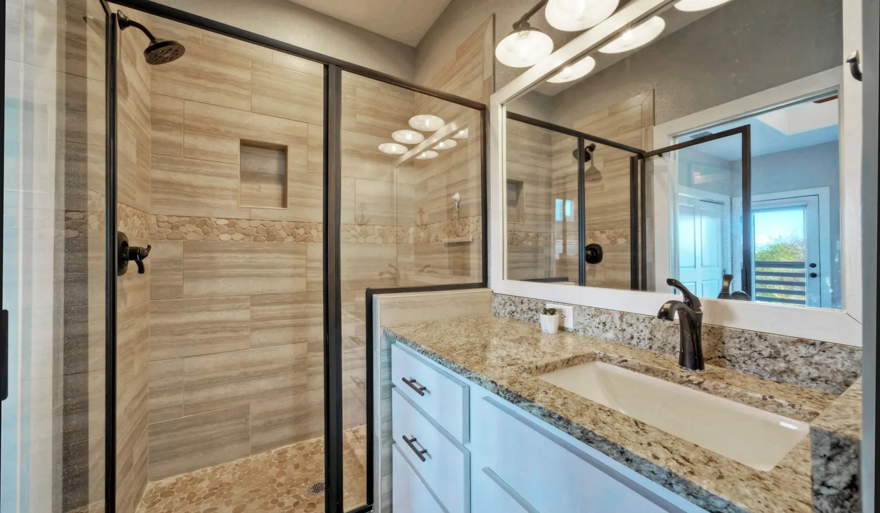 Un baño con ducha de vidrio, un espejo grande y un mueble con lavabo.