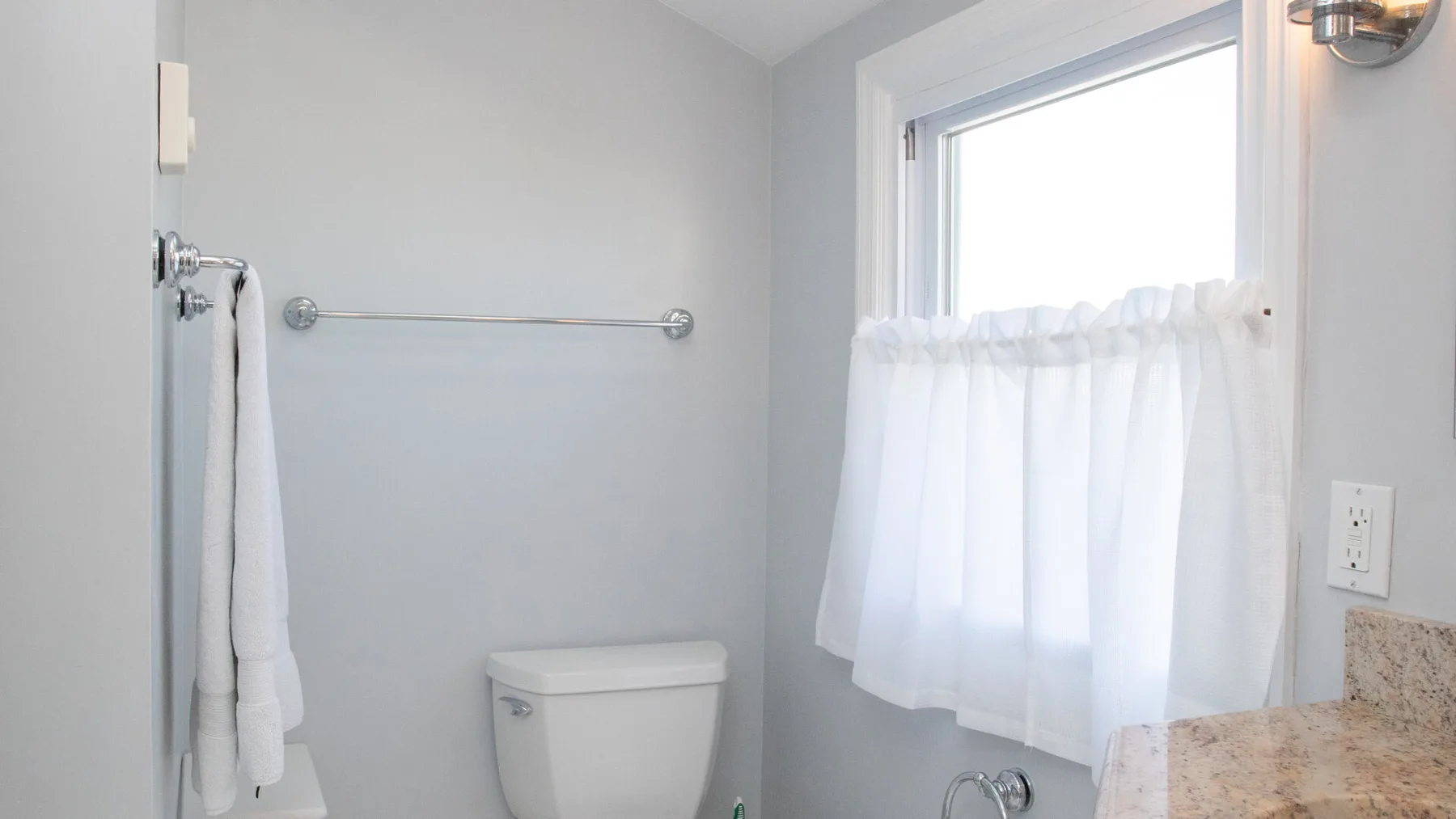 Un baño luminoso con una ventana, una barra para toallas y un inodoro.