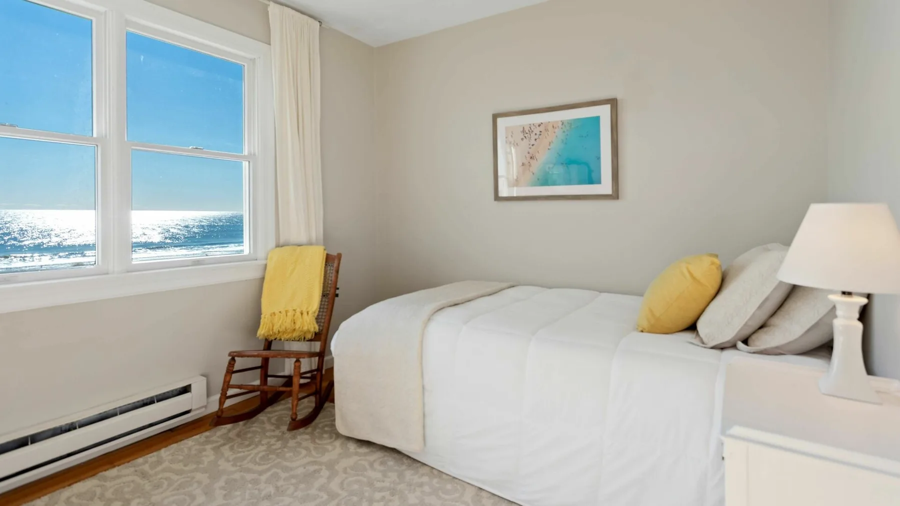 Un dormitorio luminoso con una cama blanca junto a grandes ventanas con vistas al agua.