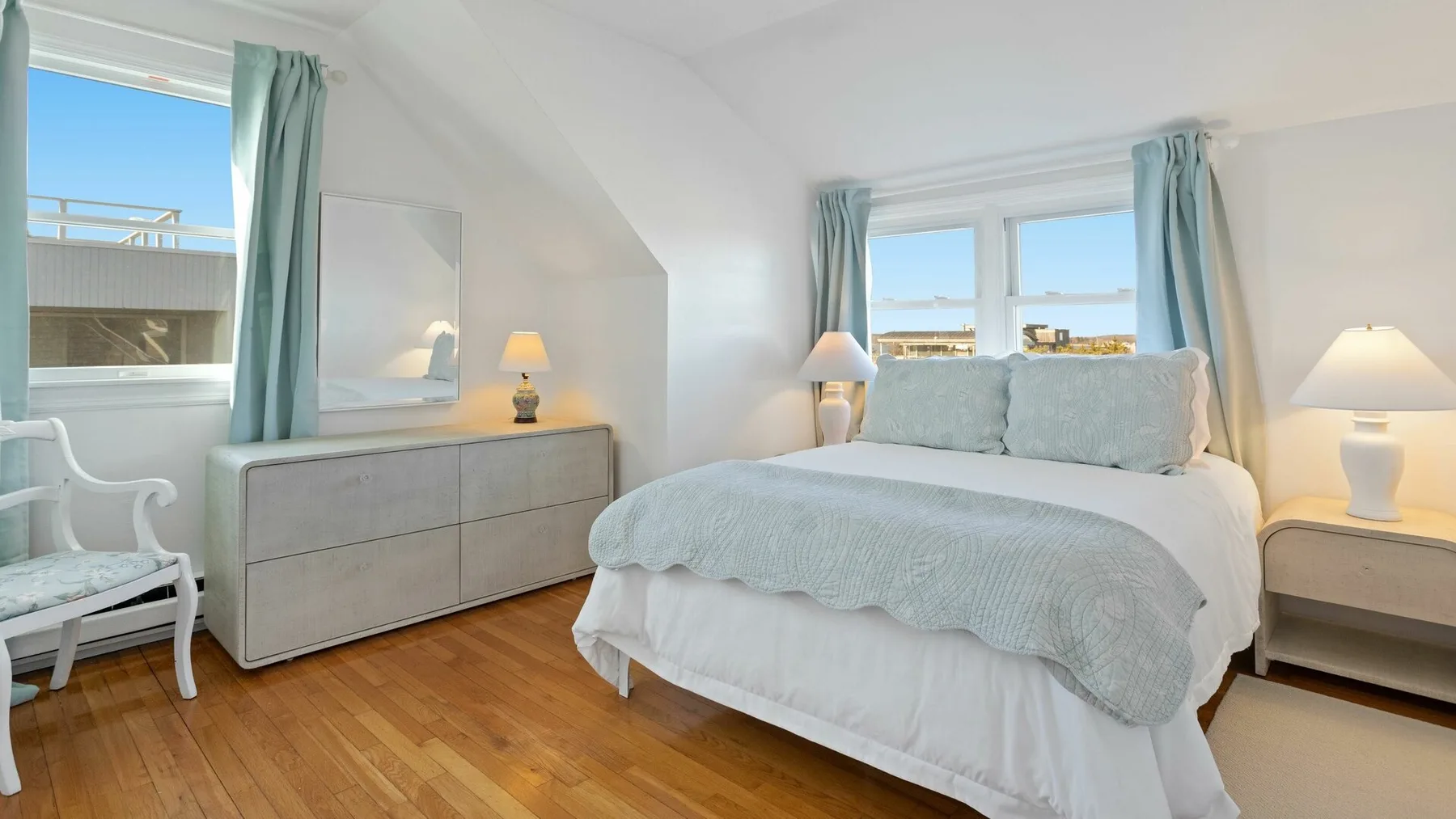 Un dormitorio luminoso con una cama tendida y ventanas con vistas al agua.