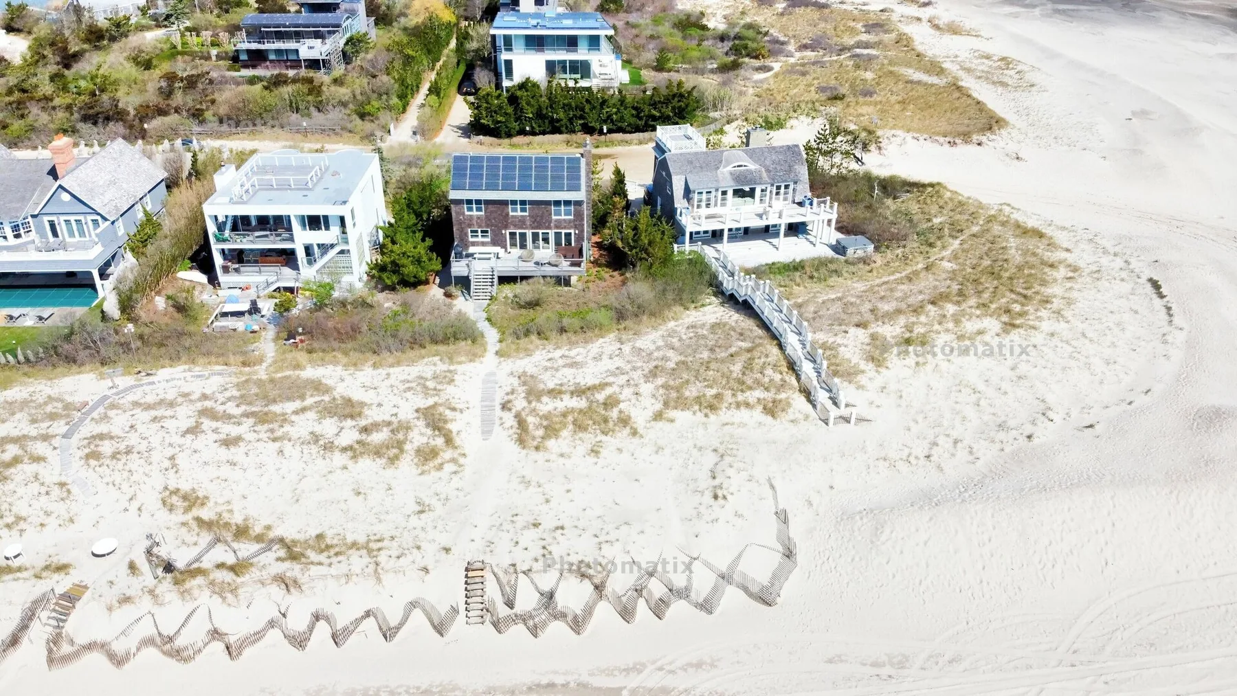 Vista aérea de varias casas junto a una playa de arena y vegetación costera.