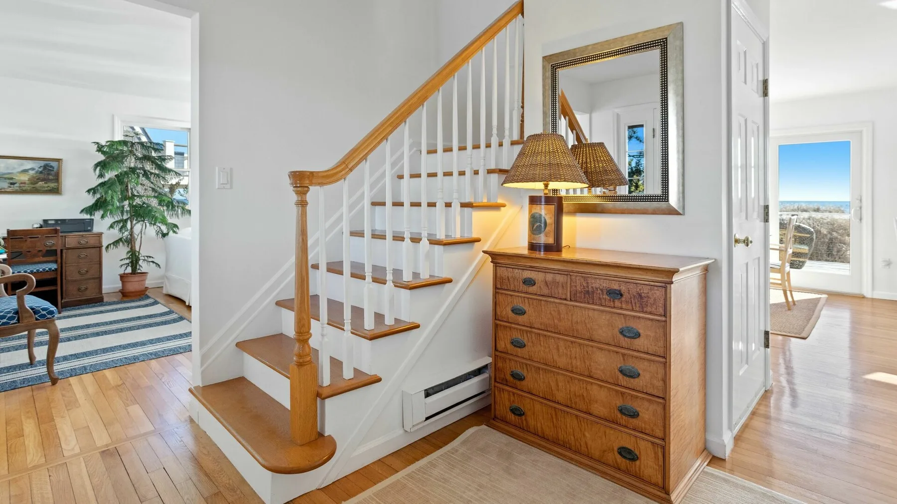 Un pasillo interior luminoso con una escalera de madera y una cómoda.