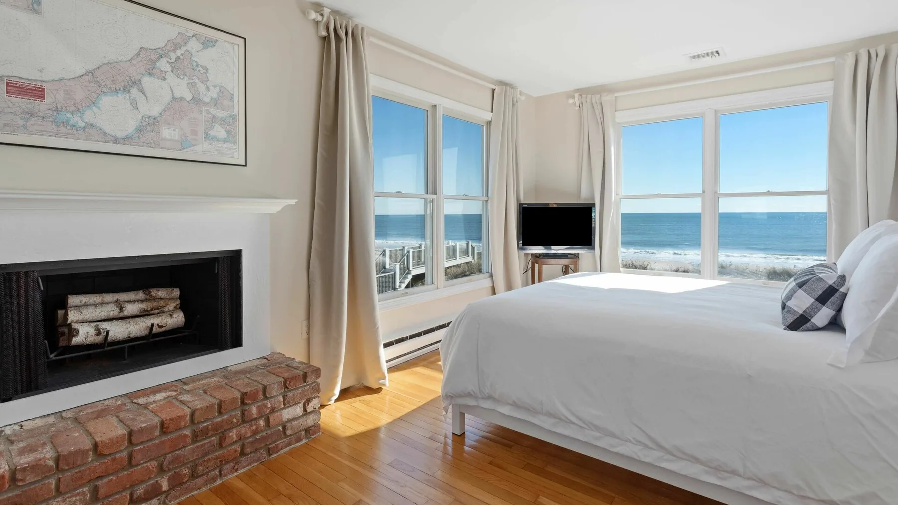 Un dormitorio luminoso con una cama blanca, una chimenea y vistas al mar por grandes ventanas.