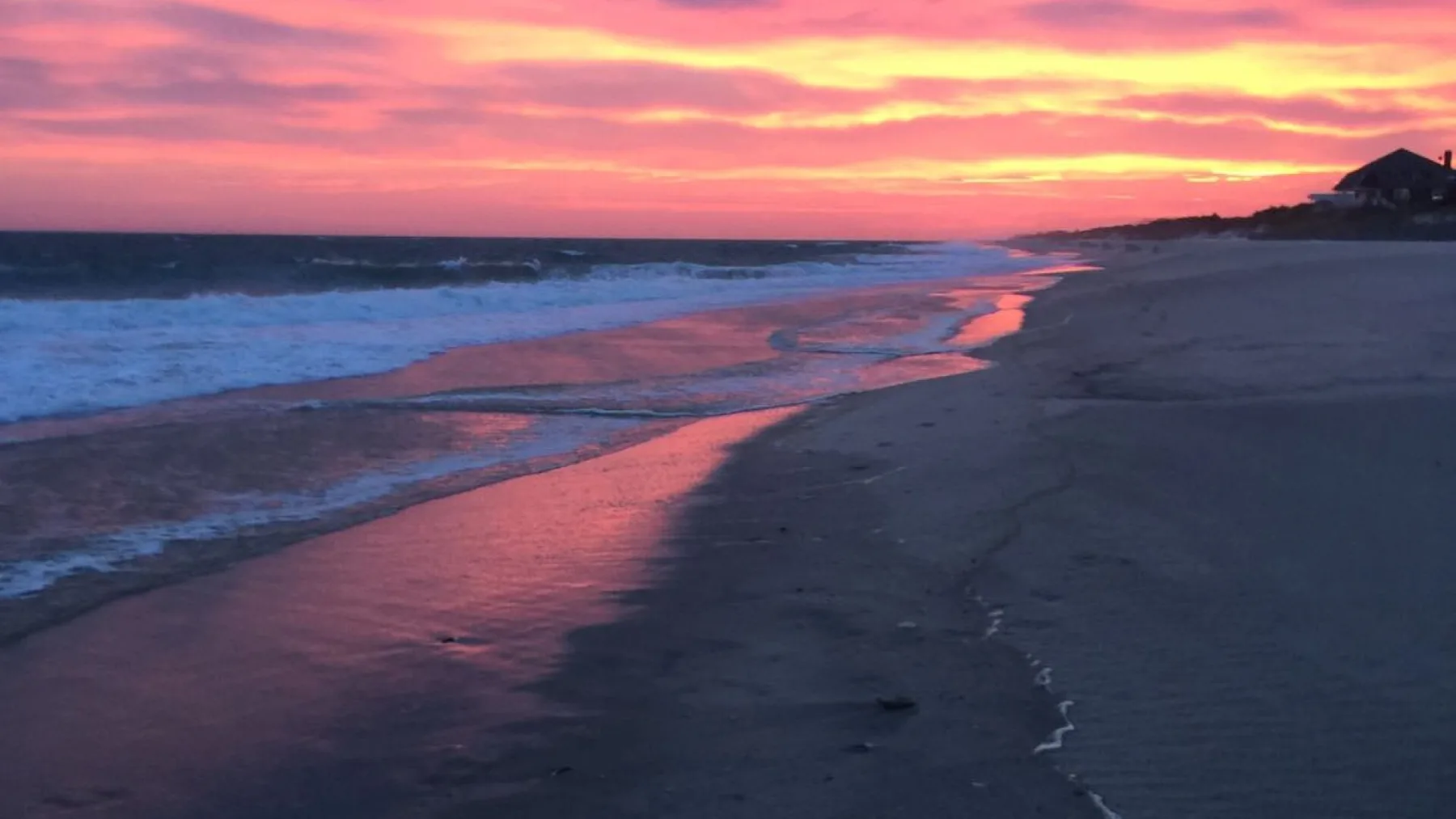 Una playa al atardecer, con luz rosada reflejada en la orilla.