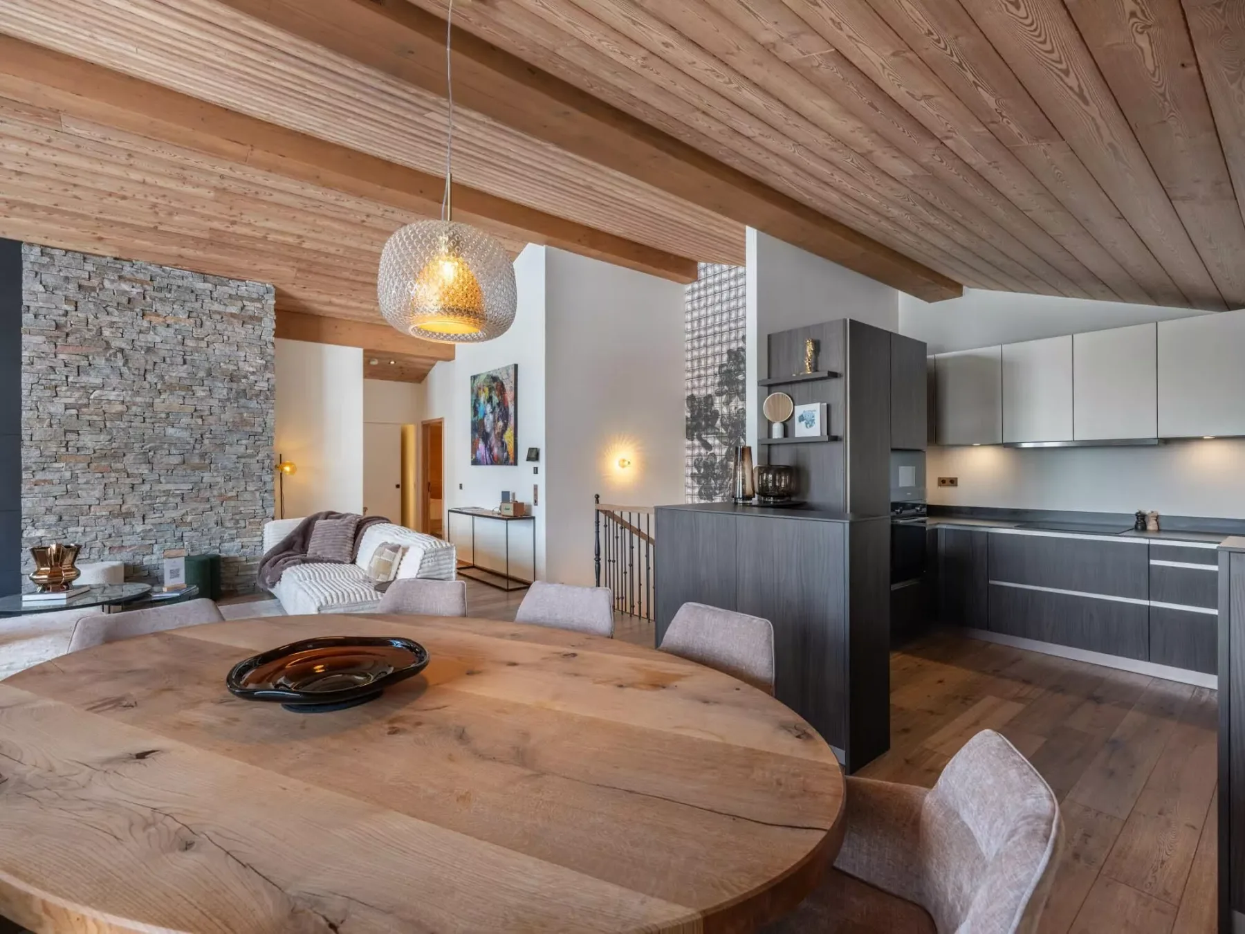 Una sala de estar y cocina de concepto abierto tiene una mesa de comedor de madera bajo un techo de madera.