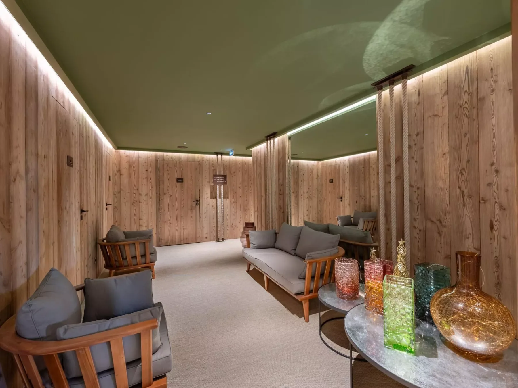 Un salón revestido de madera con asientos y recipientes de vidrio de colores sobre una mesa.
