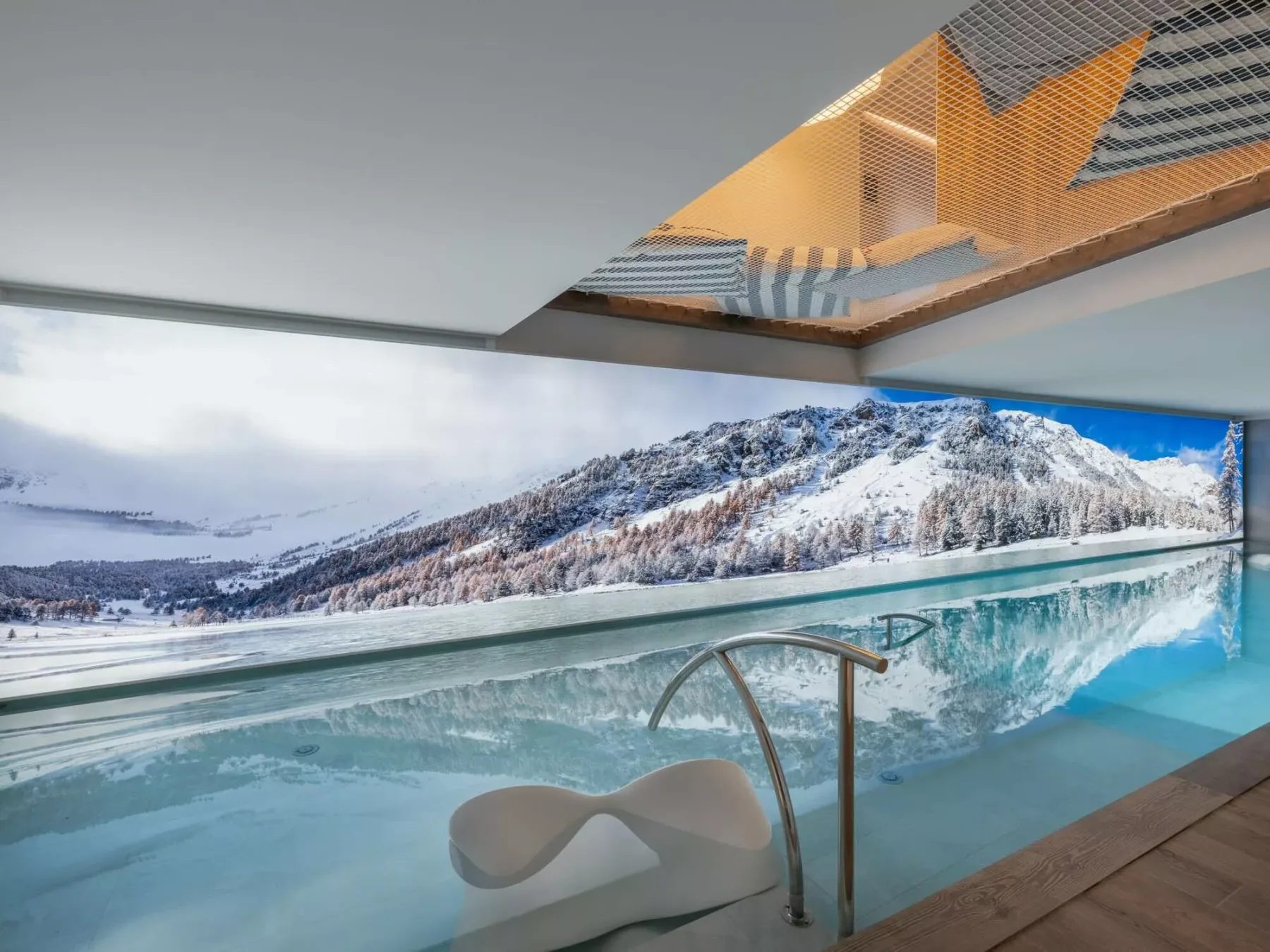 Una piscina cubierta ofrece vistas de montañas nevadas a través de un amplio ventanal.