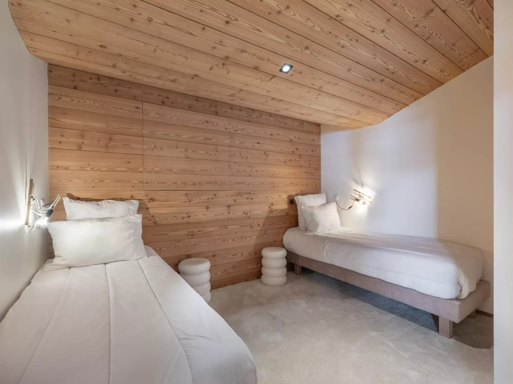 Dormitorio con dos camas, ropa de cama blanca y paredes y techo revestidos de madera.
