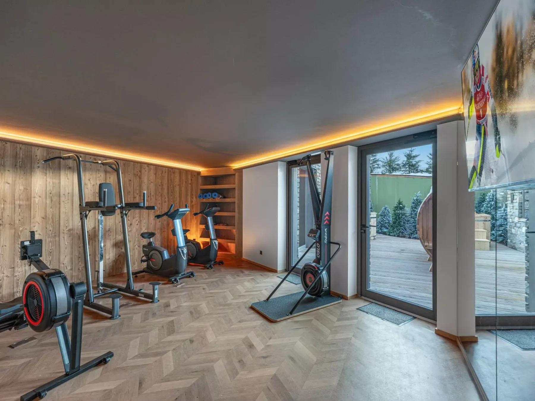 Un gimnasio en casa con equipo de ejercicio y grandes ventanas con vista a una terraza exterior.