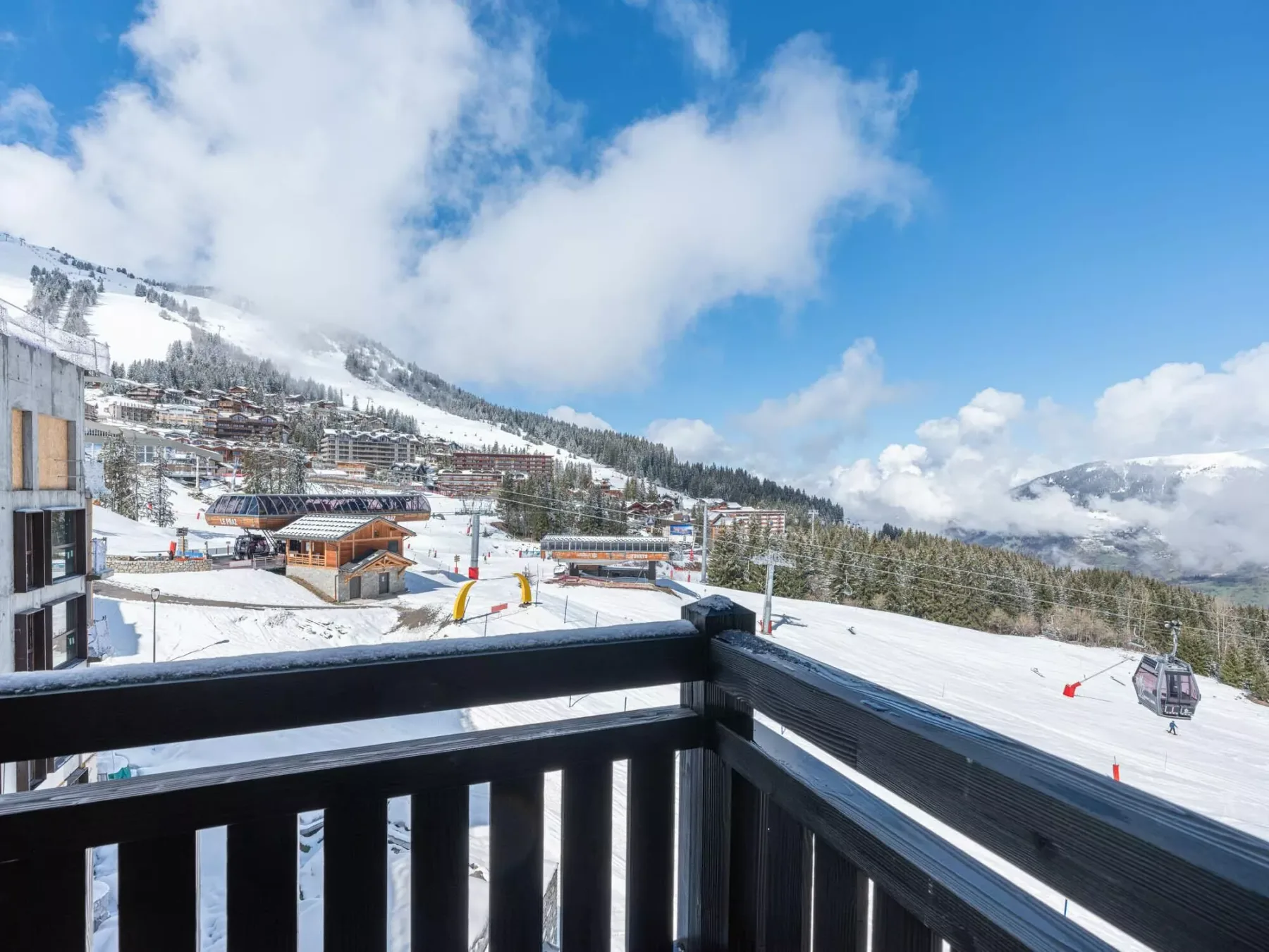 Se ven pistas nevadas y edificios de montaña más allá de una barandilla de balcón.
