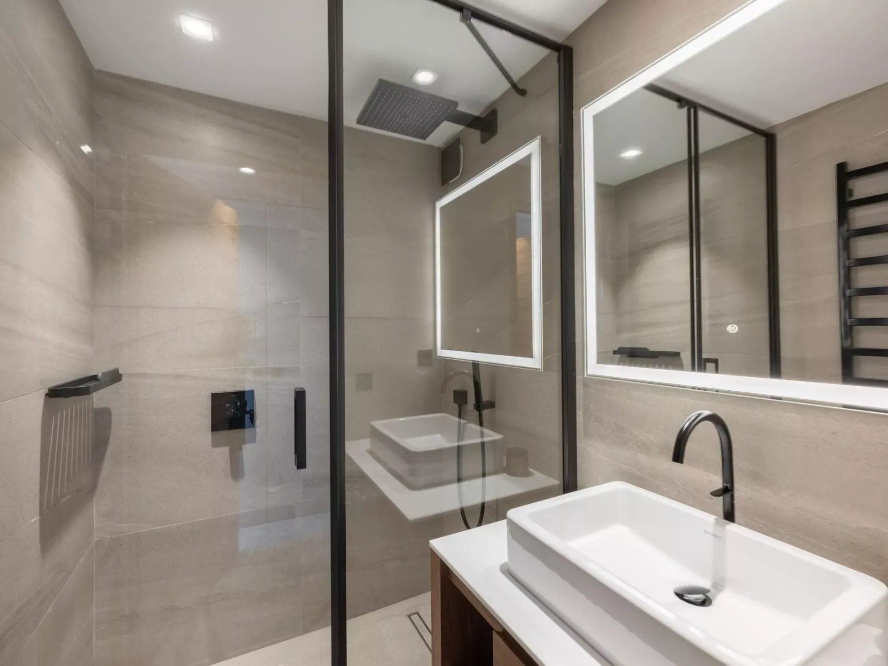 Un baño moderno con ducha de vidrio, lavabo blanco y un espejo grande.