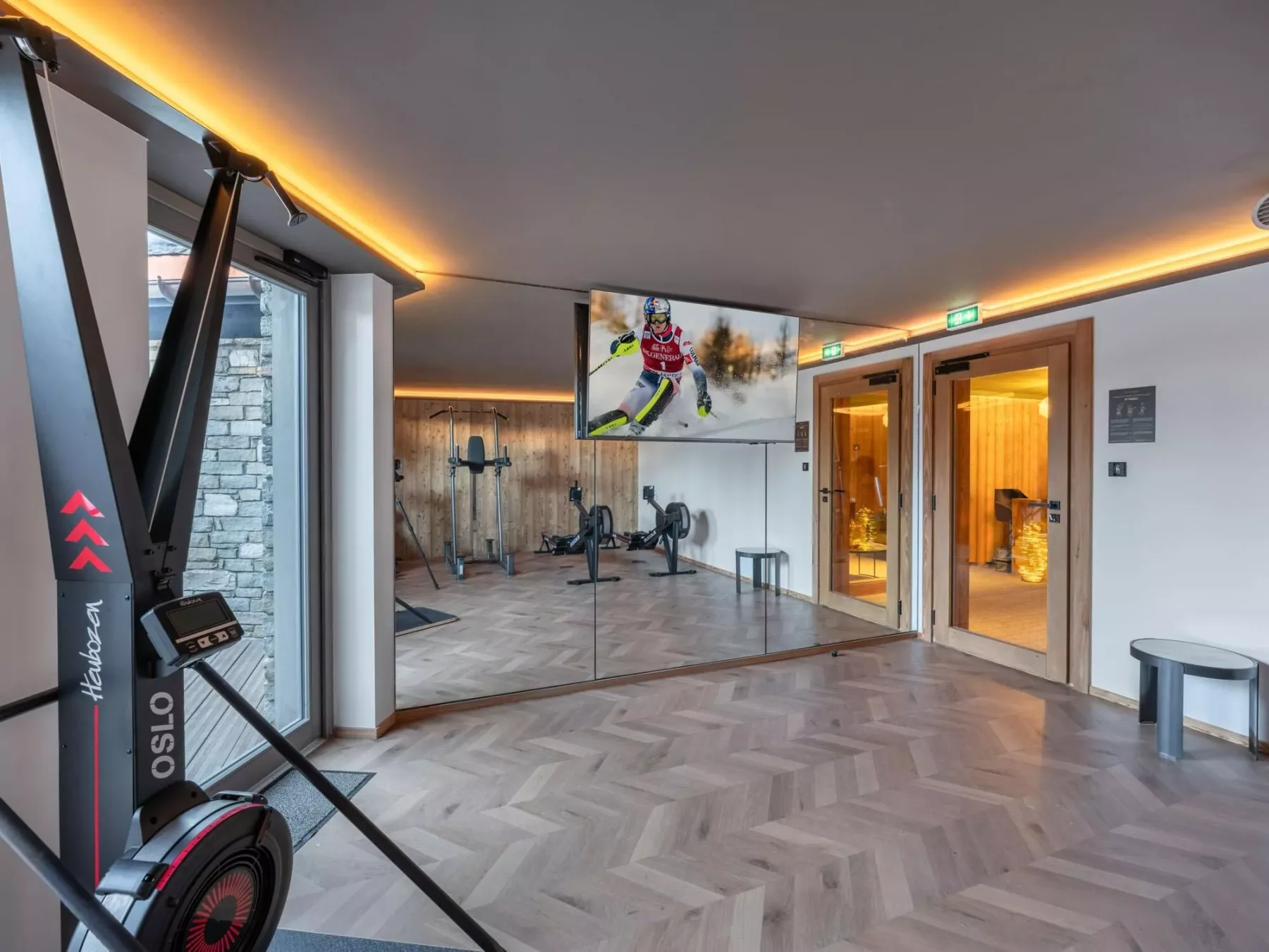 Un gimnasio con equipo de ejercicio, paredes con espejos y un televisor.