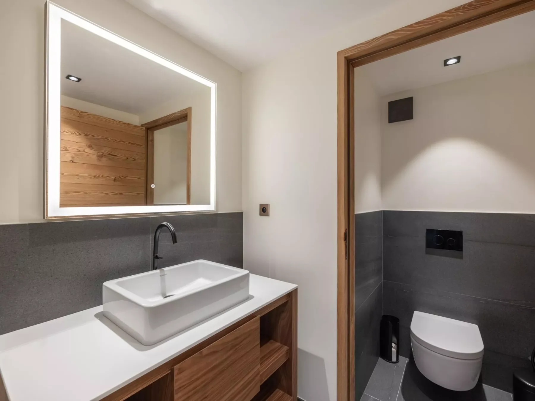 Un baño moderno con lavabo sobre encimera, espejo iluminado e inodoro.