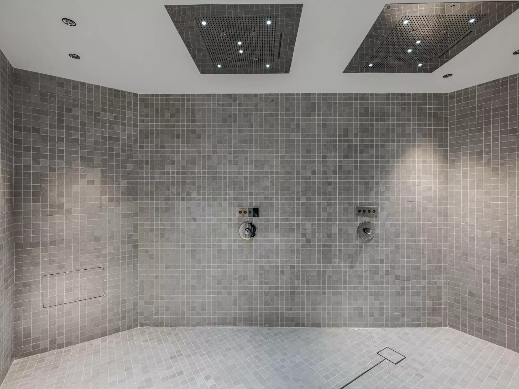 Una zona de ducha con azulejos, accesorios en la pared y luces en el techo.