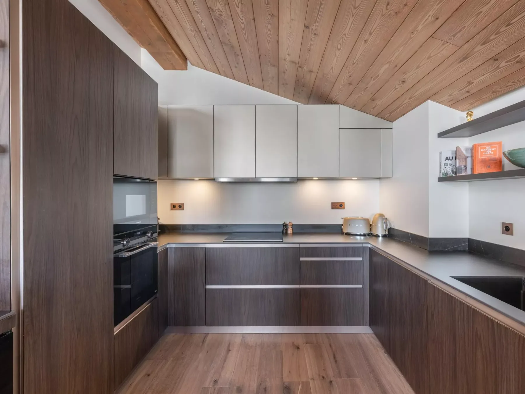 A modern kitchen with dark cabinetry, light countertops, and a wood-paneled ceiling.