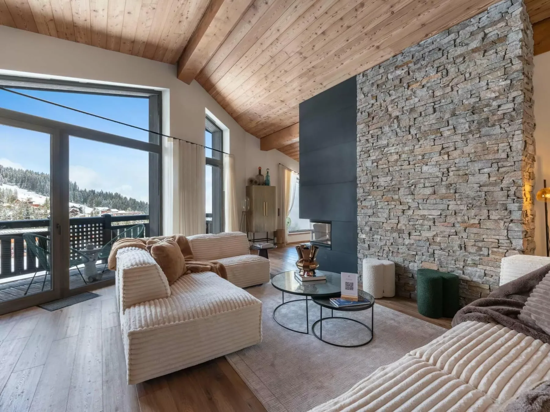 Una sala luminosa con asientos junto a grandes ventanas y una pared de piedra junto a la chimenea.