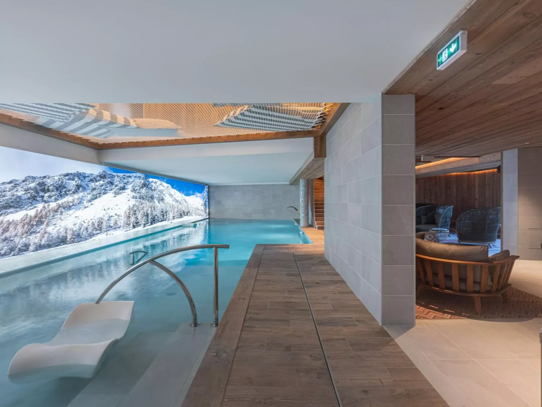 Una piscina cubierta ofrece vistas a montañas nevadas, con asientos junto al agua.